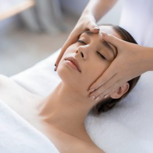 Young woman having anti-stress facial massage in salon at spa resort